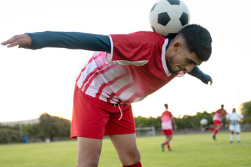 Caucasian young male player with soccer ball on back bending and balancing against clear sky