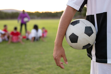 Midsection of caucasian male player in white uniform with soccer ball standing against clear sky