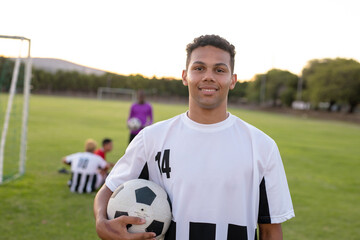 Portrait of caucasian smiling male player in white uniform holding soccer ball against clear sky
