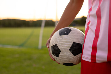 Midsection of caucasian male soccer player holding ball while standing against clear sky at sunset