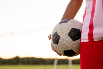 Midsection of caucasian male soccer player in red jersey holding ball standing against clear sky