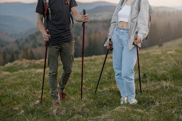 Close up of male and female legs in trekking shoes with waling sticks in hands. Travelers.