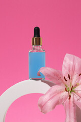 Cosmetic glass bottle with dropper for essential oils and serum on a podium with lily flower. Face and body care spa concept and natural cosmetics