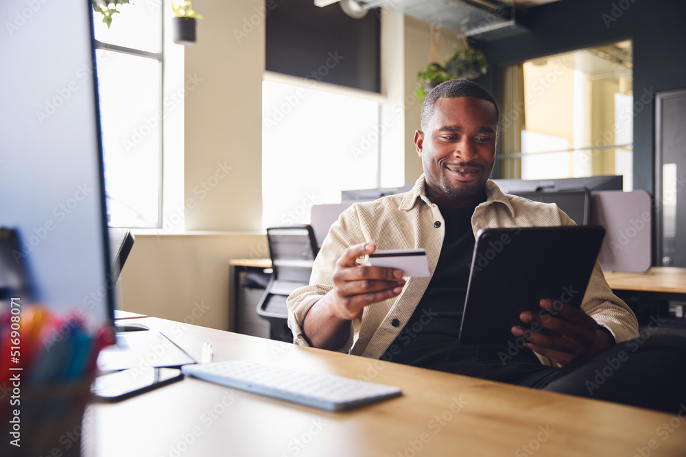 Wall mural smiling man making online payment on tablet computer holding credit card in office