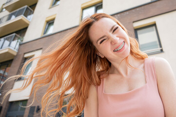 Beautiful young red-haired woman with braces on her teeth smiling in the summer outdoors