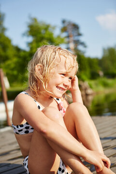 Smiling girl in swimsuit sitting on jetty