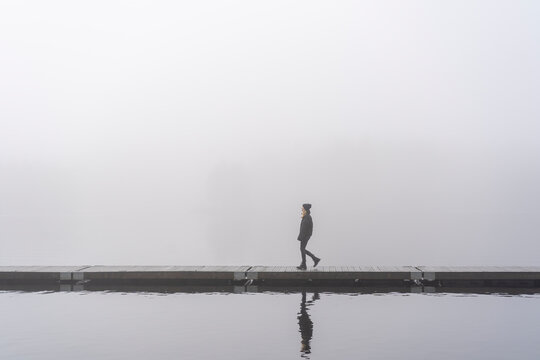 Teenage girl walking on jetty on lake under fog