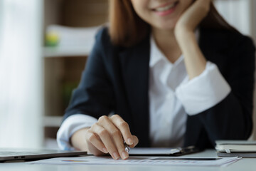 Asian woman looking at documents at a desk in a startup company, she is a financier overseeing the company's finances in accordance with policy and accuracy. Concept of corporate financial management.