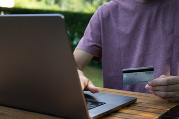 Jeune homme utilisant sa carte de crédit pour payer en ligne sur son ordinateur, vue rapprochée. Nomade numérique travaillant à l'extérieur dans la nature