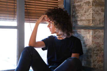 Beautiful woman sitting on the edge of a large window in her studio while making different expressions of joy and depression. Concept of different moods.