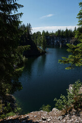 Fototapeta premium The concept of travel in Russia. Ruskeala Mountain Park in summer, Karelia. A popular tourist destination. Marble Canyon. Clear turquoise water in the lake and a rowing boat in the distance.