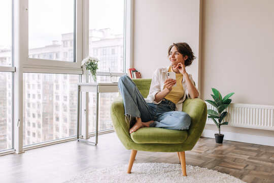 Caucasian brunette woman sitting in home . Full view of pretty young woman looking and smiling at mirror on the green chair. Concept of home mood, relax 
