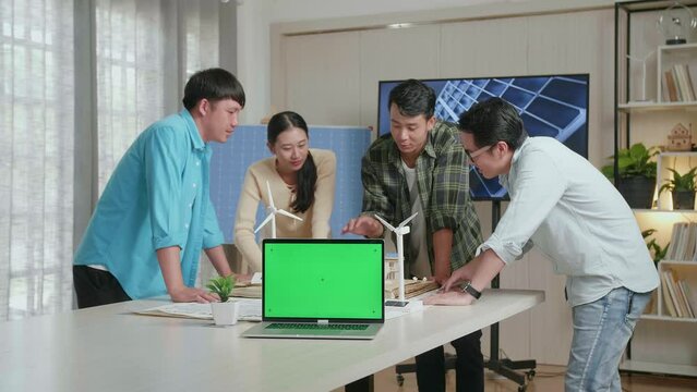 Green Screen Laptop On The Table While Asian Engineers Group Discussing About Small House Model With Solar Panel At The Office
