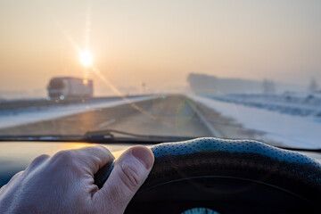 view of the driver hand on the steering wheel of the car while driving on a slippery snow covered road - obrazy, fototapety, plakaty