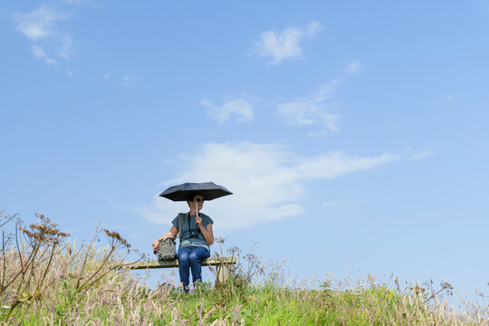 Senior woman with umbrella sitting on bench on hill