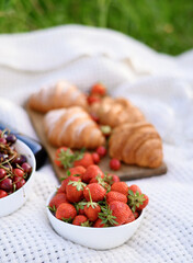 Strawberries on a plate on the background of a white blanket on a picnic in a green field with croissants