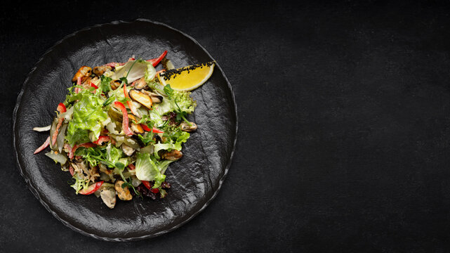 Salad with mussels, on a black plate
