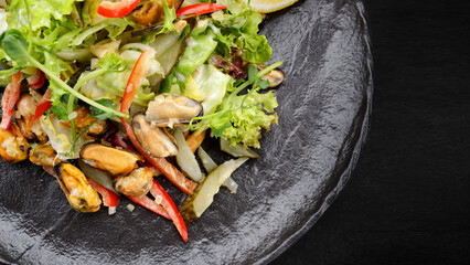 Salad with mussels, on a black plate