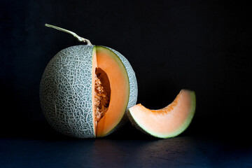 Whole and sliced Japanese melons, honey melon or cantaloupe on black isolated background, copy space. Summer fruits.