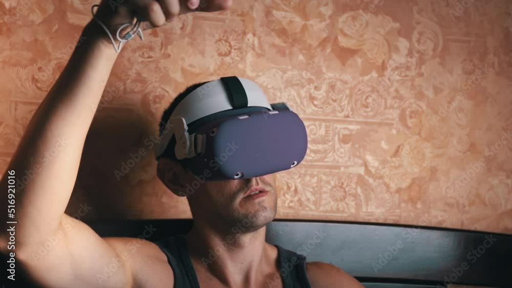 Poster man in a virtual reality helmet controls the controllers. a young man at home sitting on a bed is in