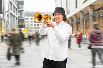 Young caucasian long-haired blond man in white shirt and hat playing funky jazz on golden trumpet...