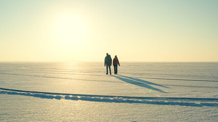 Fototapeta na wymiar The two travelers with backpacks trekking through the snow field