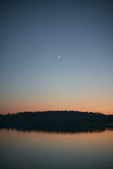 Crescent in the evening sky over beautiful lake in the summer evening. Concept of outdoor nightstand.
