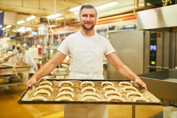 Bäcker Lehrling trägt Backblech mit Croissants