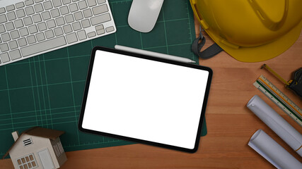 Naklejka premium Digital tablet, protective helmet and blueprints on a wooden table. Engineer, Architect office desk