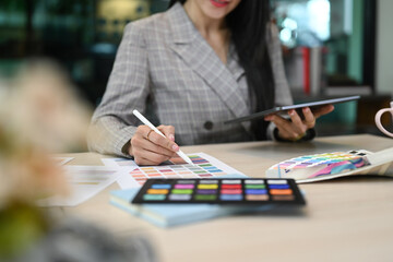 young woman interior designer working with color swatches and using digital tablet at her workplace