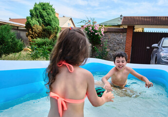 Happy school age kids play ball and splashing each other with water in inflatable swimming pool during summer holidays