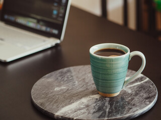 A cup of coffee on a marble board. Home office, coffee time, laptop.