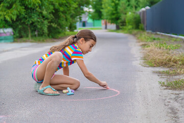 The child draws with chalk on the pavement. Selective focus.
