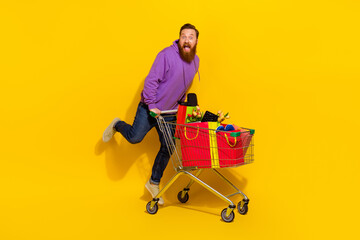 Full size photo of excited overjoyed person jump full shopping cart gifts isolated on yellow color...