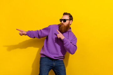 Photo of cool excited man wear violet sweatshirt dark glasses dancing pointing empty space isolated...