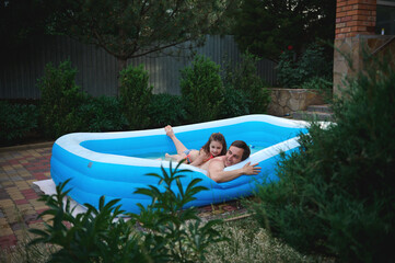 Cute little girl is playing water games with her loving father in the inflatable pool in the backyard garden at home