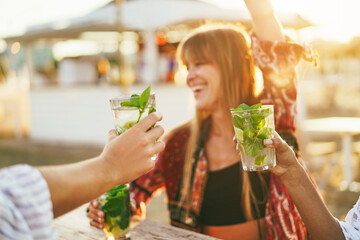 Happy girls having fun drinking alcohol free mojito at cocktail bar on the beach - Focus on right...