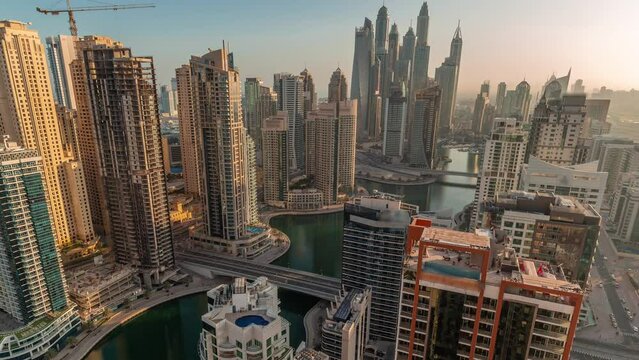 Panorama of various skyscrapers in tallest recidential block in Dubai Marina during sunrise aerial timelapse with artificial canal. Many towers and yachts early morning