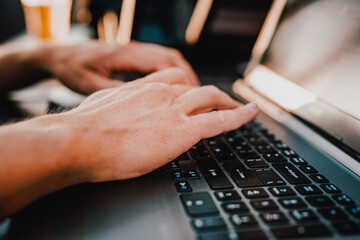 close up shot of a young mans hands typing something on a gray laptop