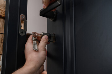 The master installs the core for the door lock, installation work with the door. - obrazy, fototapety, plakaty