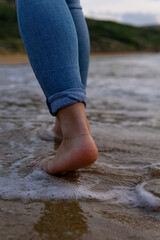 Detail of the feet of an unrecognizable woman dressed in jeans and walking along the shore with wet feet.