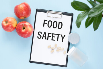 Food safety text on a paper tablet with pills lying on a blue table with apples. Can be used as concept photo