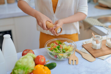Obraz na płótnie Canvas Pretty young woman chef putting salt in a salad