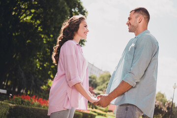 Profile portrait of two idyllic cheerful partners hold arms look each other enjoy good mood date outside