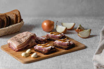 rustic natural food, on a linen tablecloth a wooden board, on it are ready-made sandwiches from black rye bread and lard with mustard and boiled eggs.