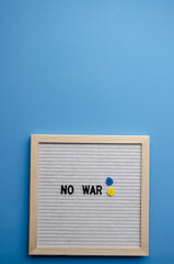 Flatlay vertical composition with a blue background, a letter board in a wooden frame with the phrase NO WAR and small hearts, blue sticker and blank blue background