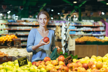 woman picks chooses fruits vegetables on the counter in supermarket. Female housewife shopping in market standing near vegetable department store with a basket in hands. Examines apple