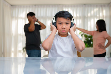 Asian boy kid wearing headphones and play loud music. so as not to hear quarrel while parents having fight or quarrel conflict at home. Unhappy problem in family, Domestic problems in the family.