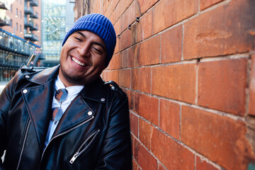 Latin Man with perfect teeth smiling standing next to the red brick wall