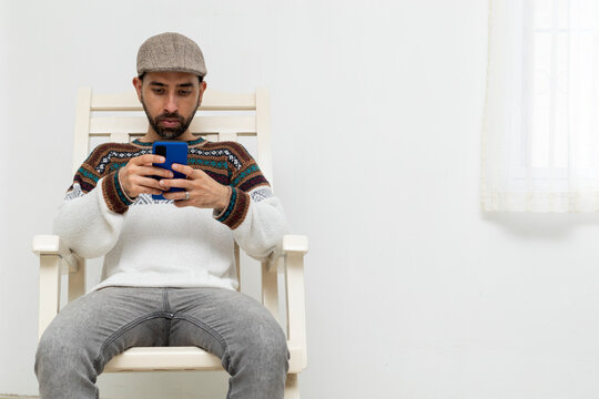Latin American man sitting on a chair in his house with his cell phone
